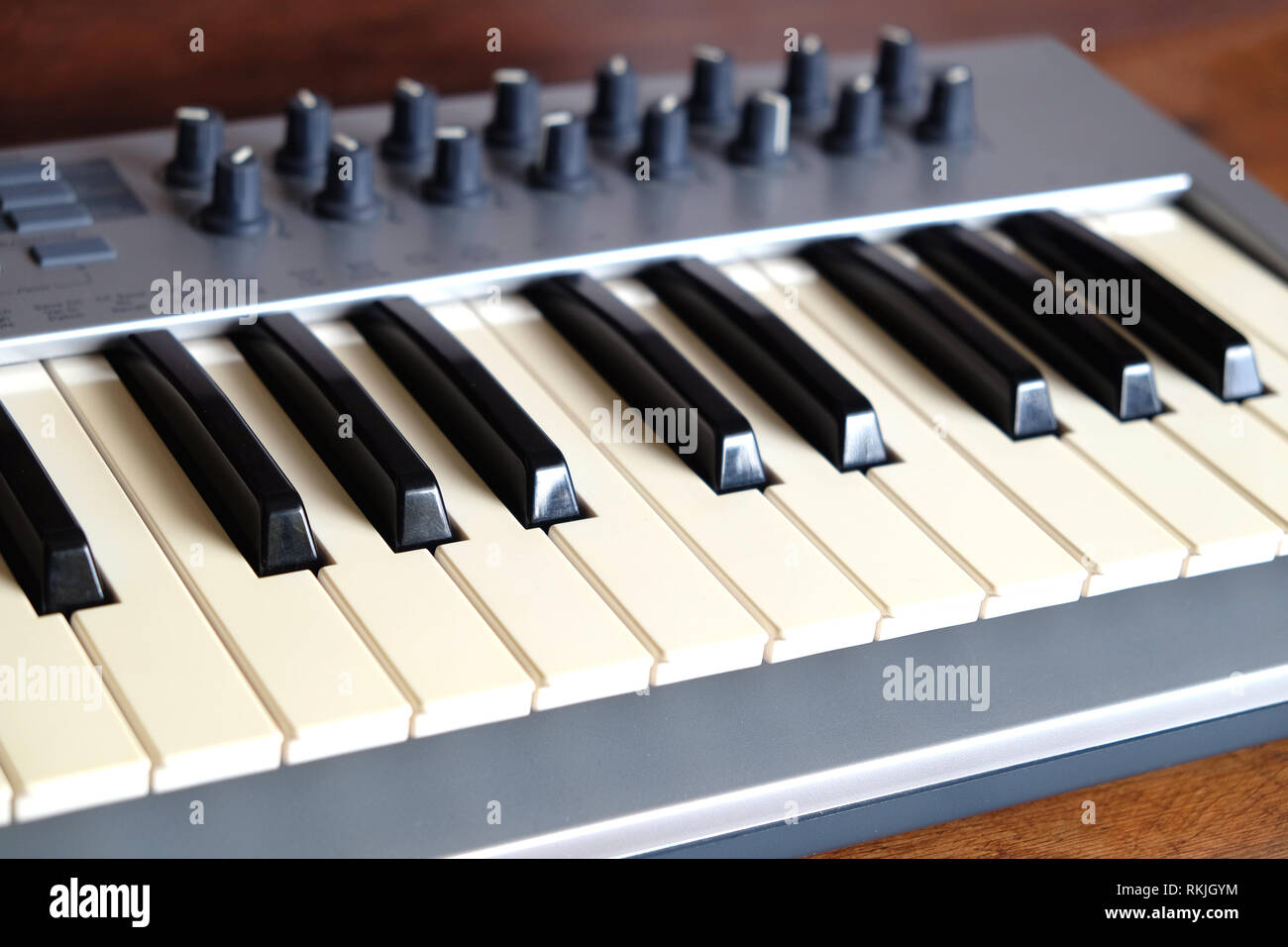 Electronic synthesizer keyboard with many control knobs in silver plastic body on wooden background side view closeup Stock Photo