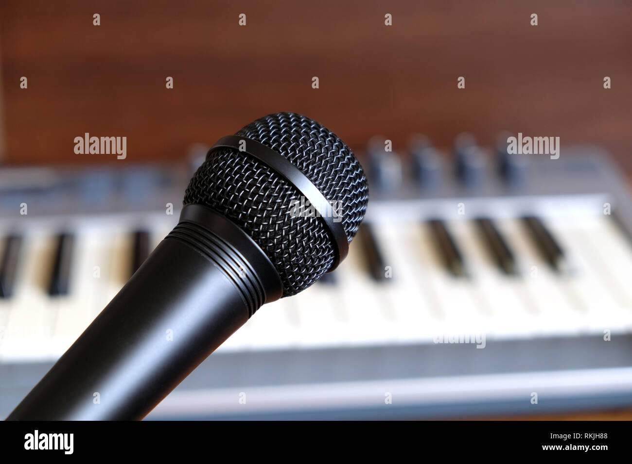 Black vocal microphone close up against defocus electronic synthesizer keyboard with many control knobs in silver plastic body as background Stock Photo