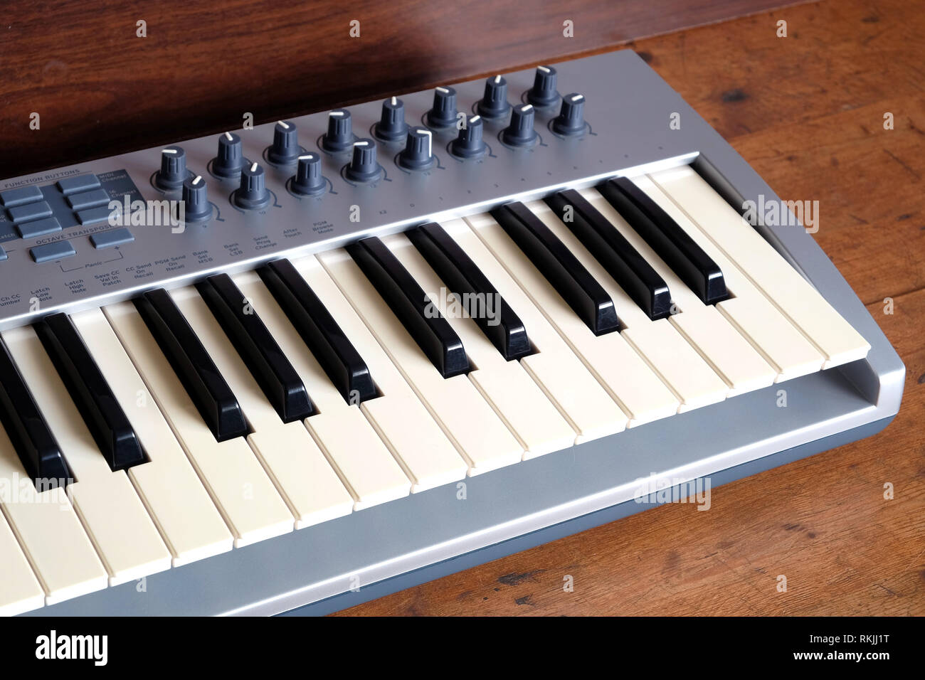 Electronic synthesizer keyboard with many control knobs in silver plastic body on wooden