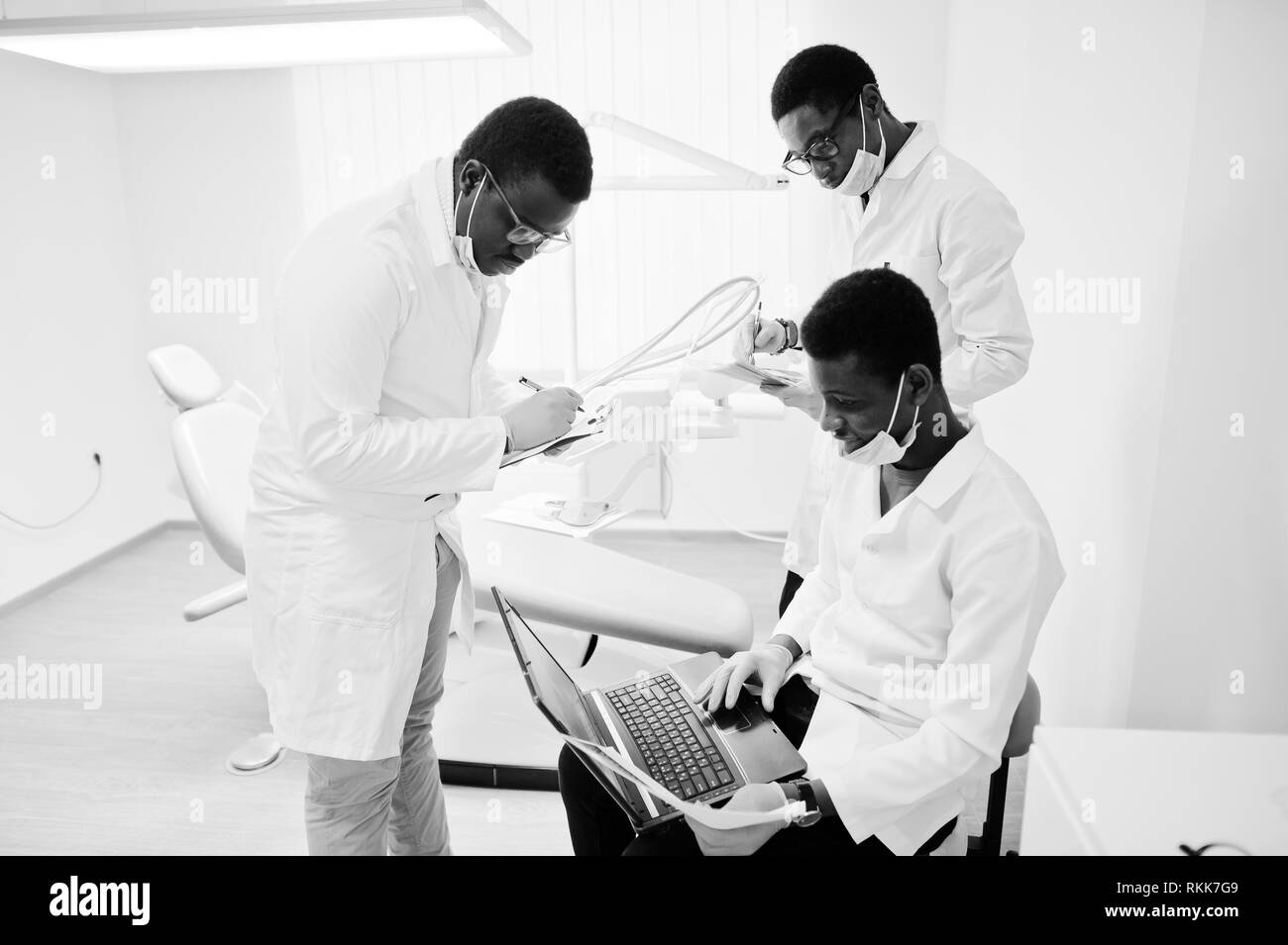 Three african american male doctors working with laptop, discussing with colleagues in dental clinic. Stock Photo
