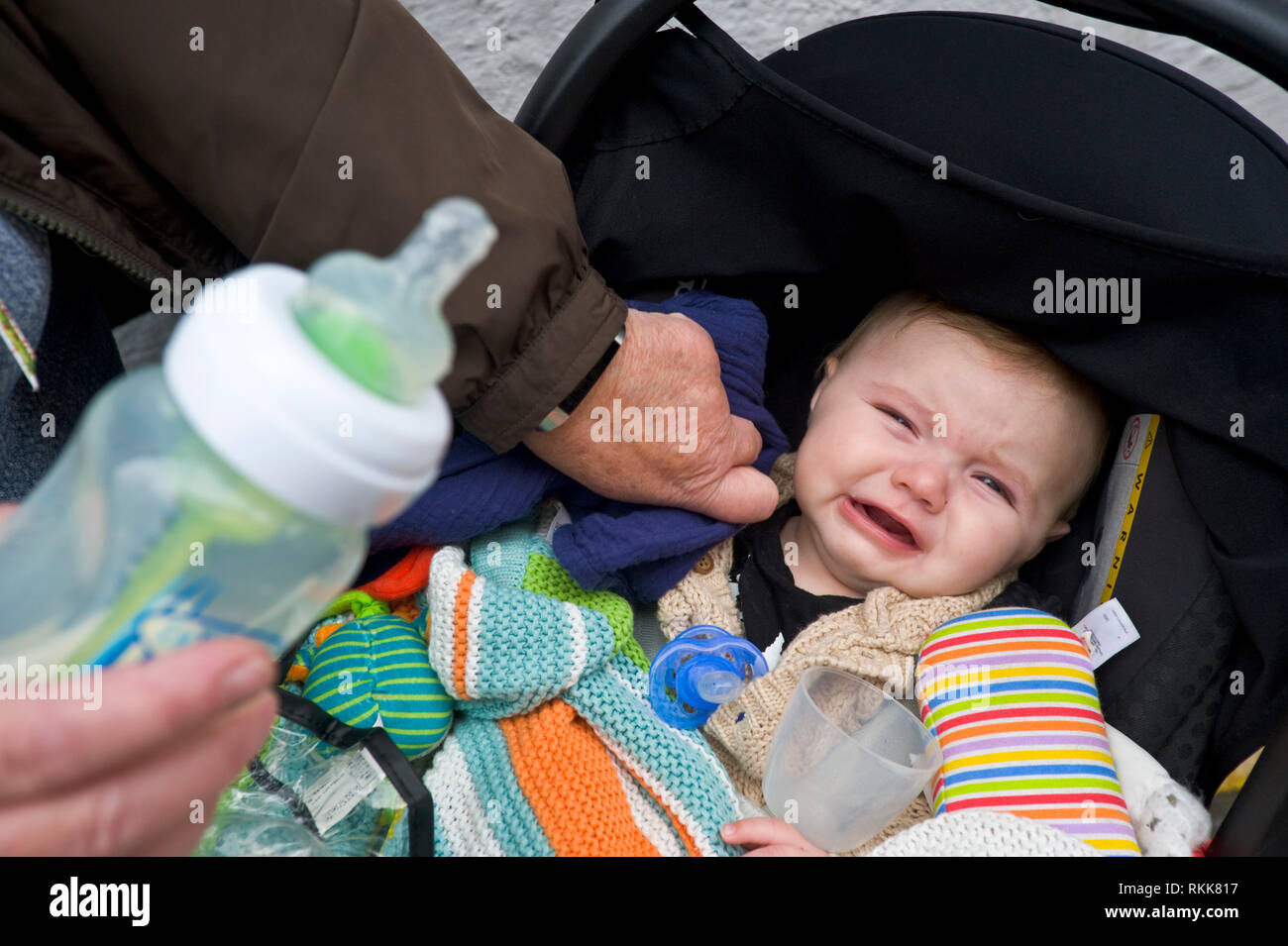 Baby in pushchair crying waiting for a bottle of milk. Stock Photo