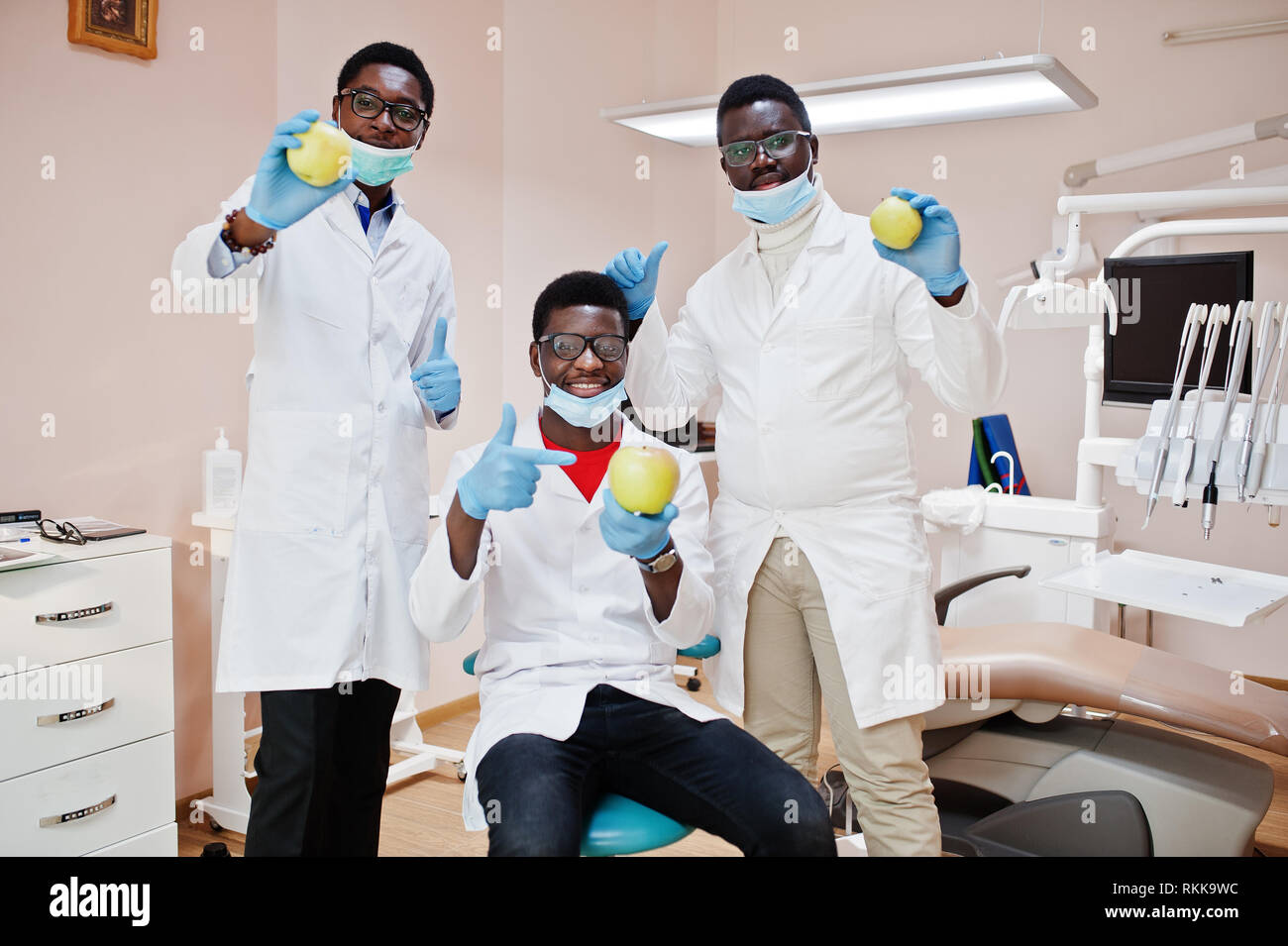 Healthy teeth are the key to happiness! Three african american male doctors colleagues in dental clinic with an apples in hands. Stock Photo