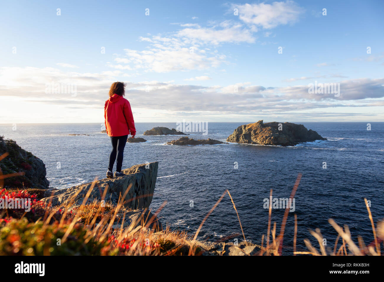 Woman in red jacket is standing at the edge of a cliff enjoying the ...