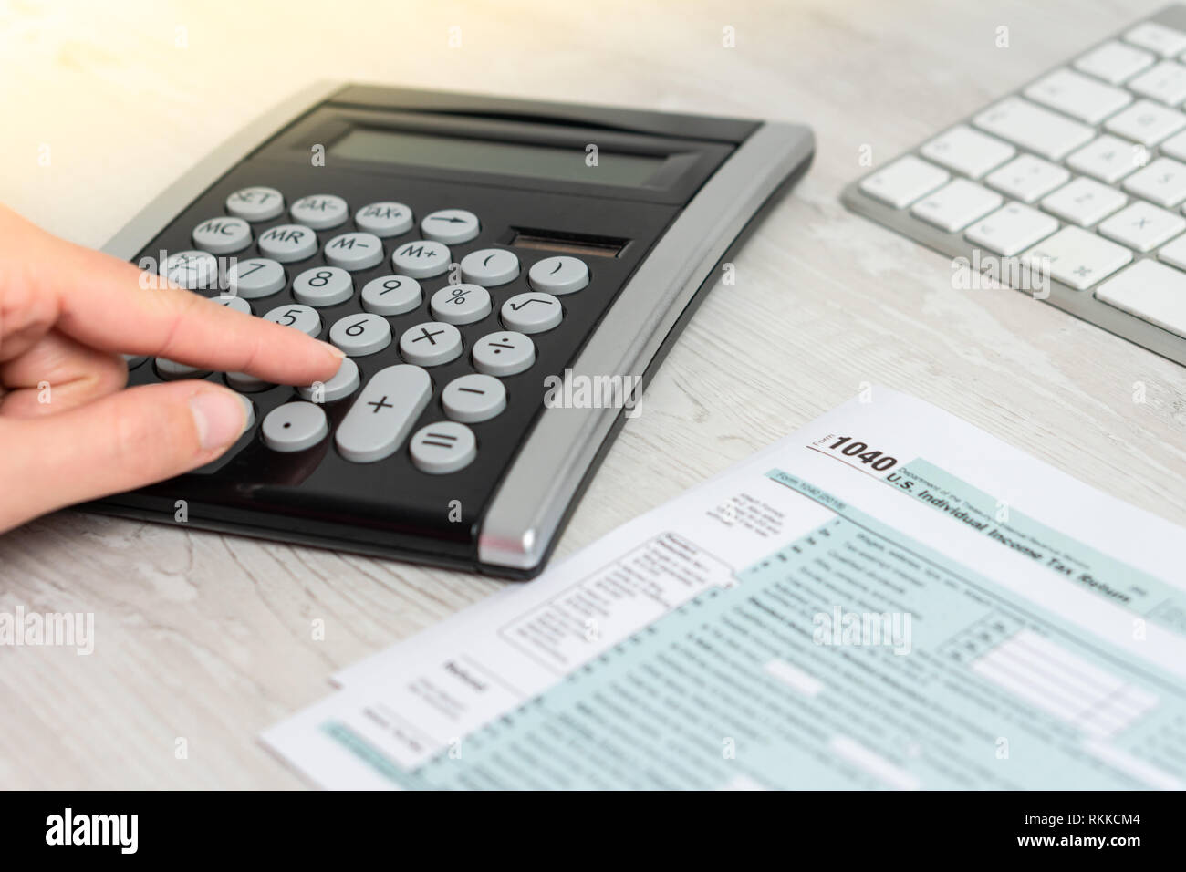 Hands calculating US tax form next to computer keyboard and tax form 1040. tax form us business income office hand fill concept Stock Photo