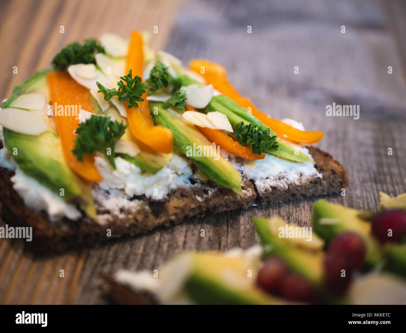 Delicious and healthy avocado toast with pomegranate, bell pepper and almond on rustic wooden board Stock Photo
