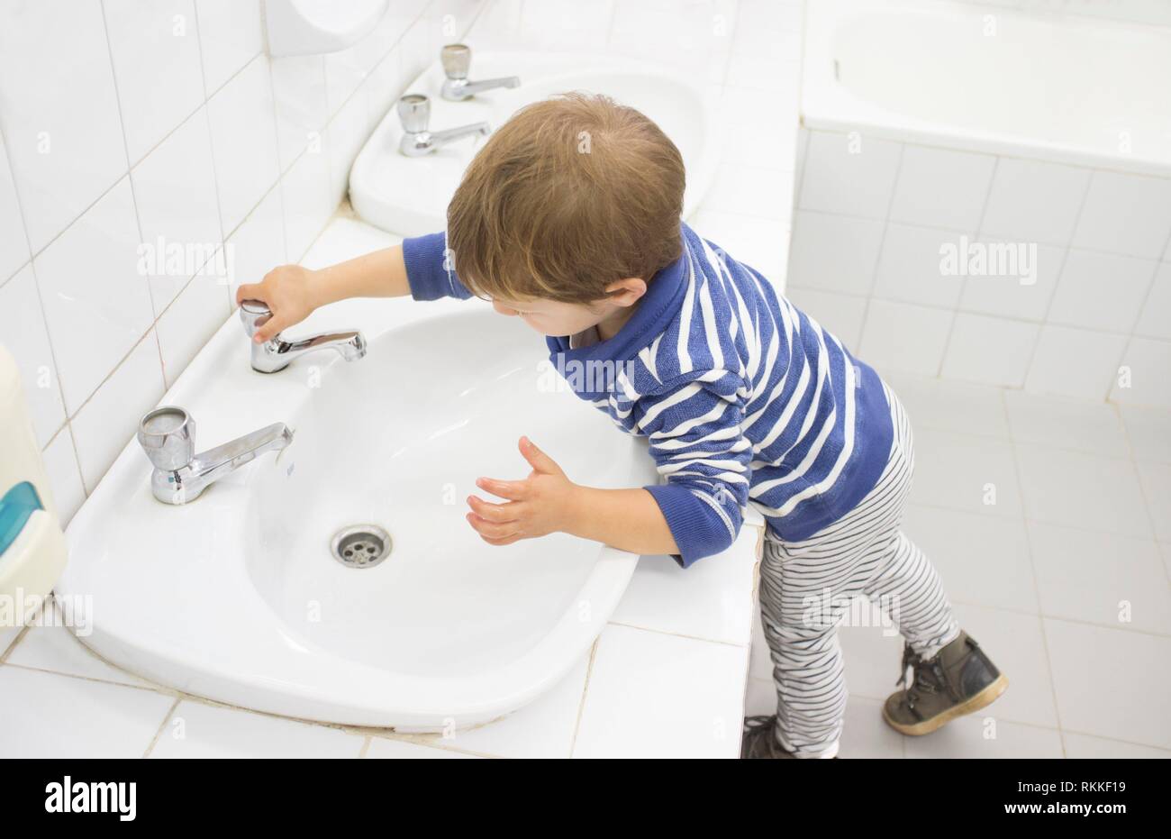 3 years boy washing hands at adapted school sink. Learning hygiene habits. Stock Photo