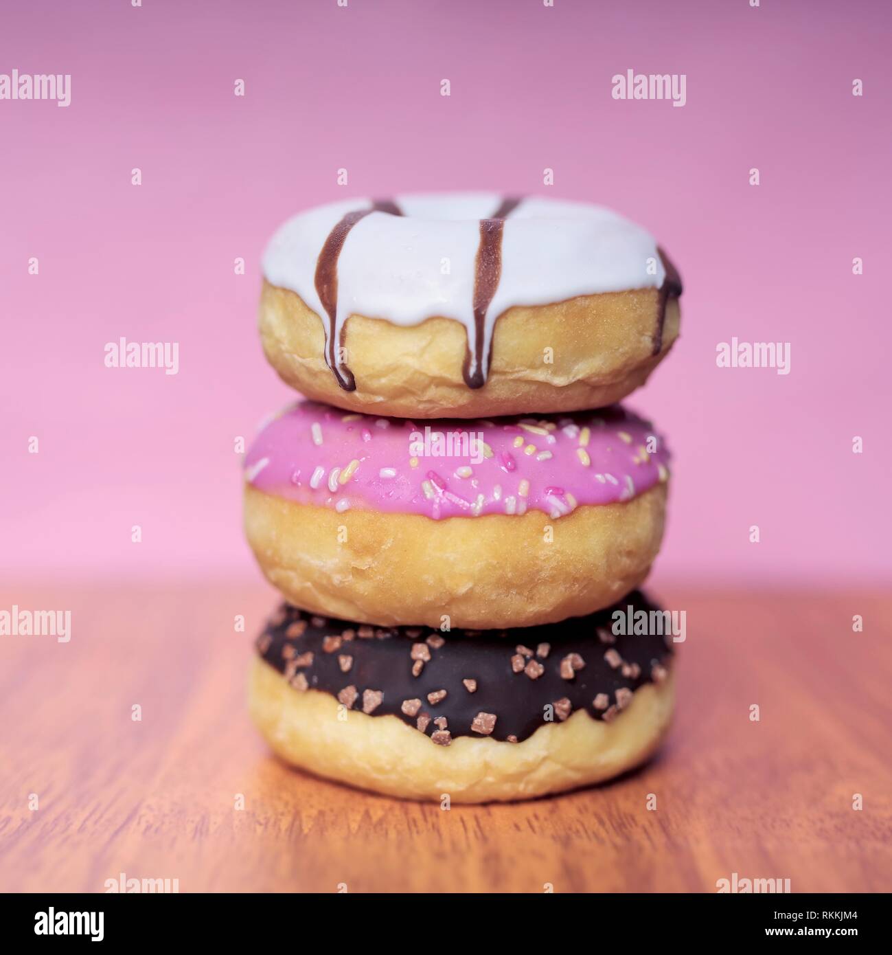 Stack of sweet glazed doughnuts on pink background. Stock Photo