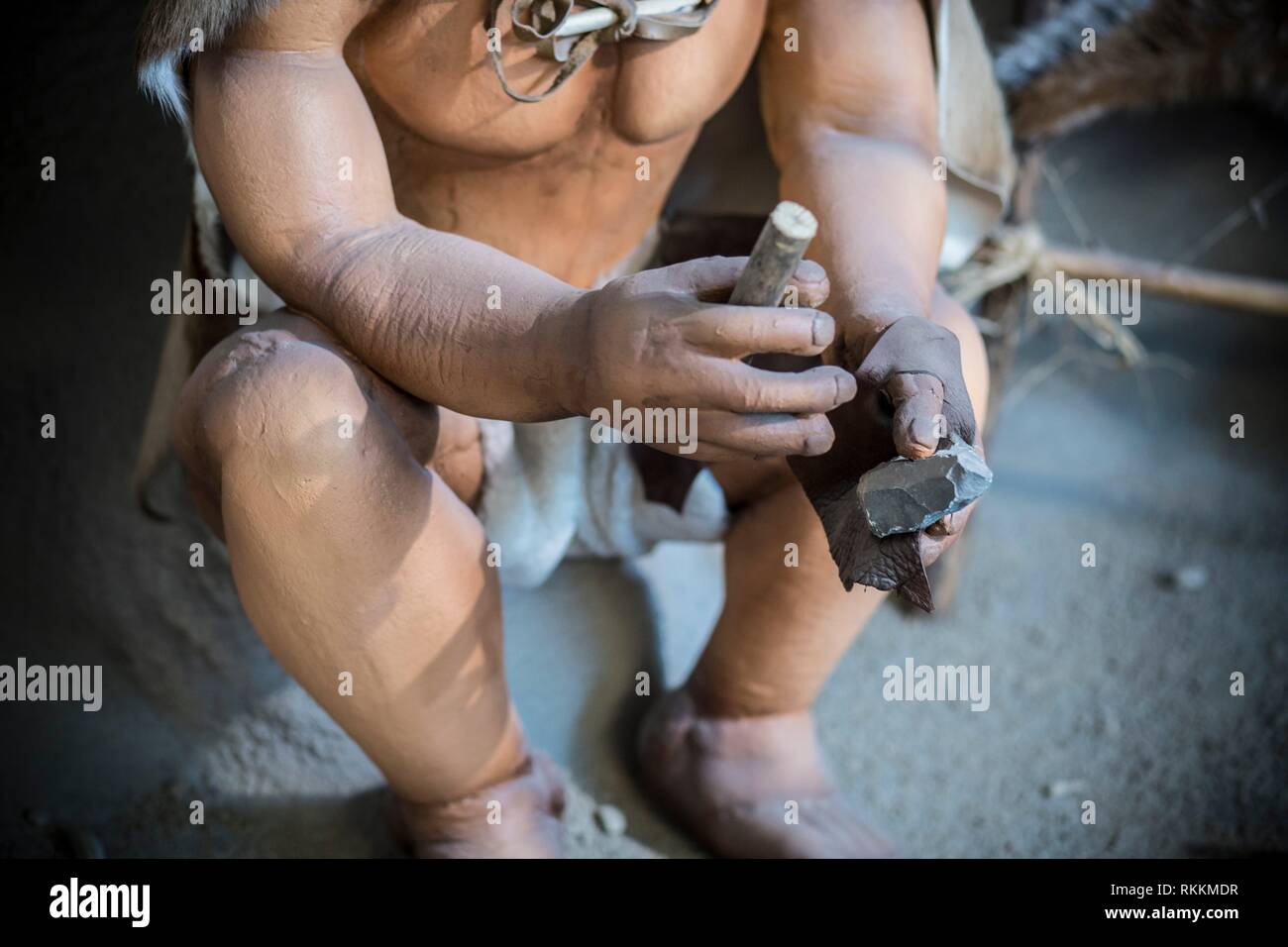 Life-sized sculpture of prehistoric man creating lithic tool Stock Photo