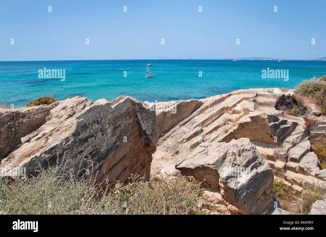 Coastal rock landscape and small boats in turquoise sea with horizon on a sunny summer day in Mallorca, Spain. Stock Photo