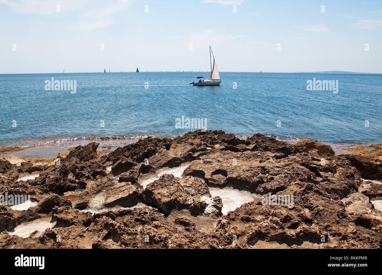 Beautiful natural coast landscape with salt cavities in rocks and sailboat in turquoise blue water in Mallorca, Spain. Stock Photo