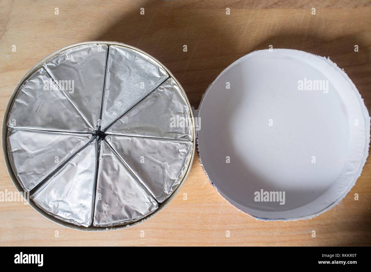 Round cardboard box with melted cheese in aluminium foil and lid on wooden table. Top view. Stock Photo