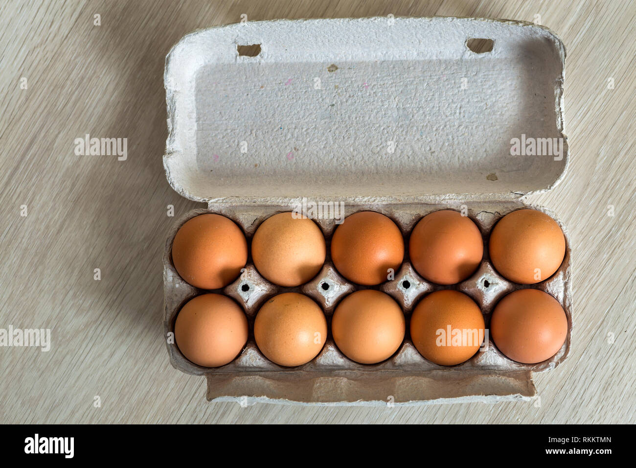 Hen eggs in open cardboard egg carton on kitchen table light copy space