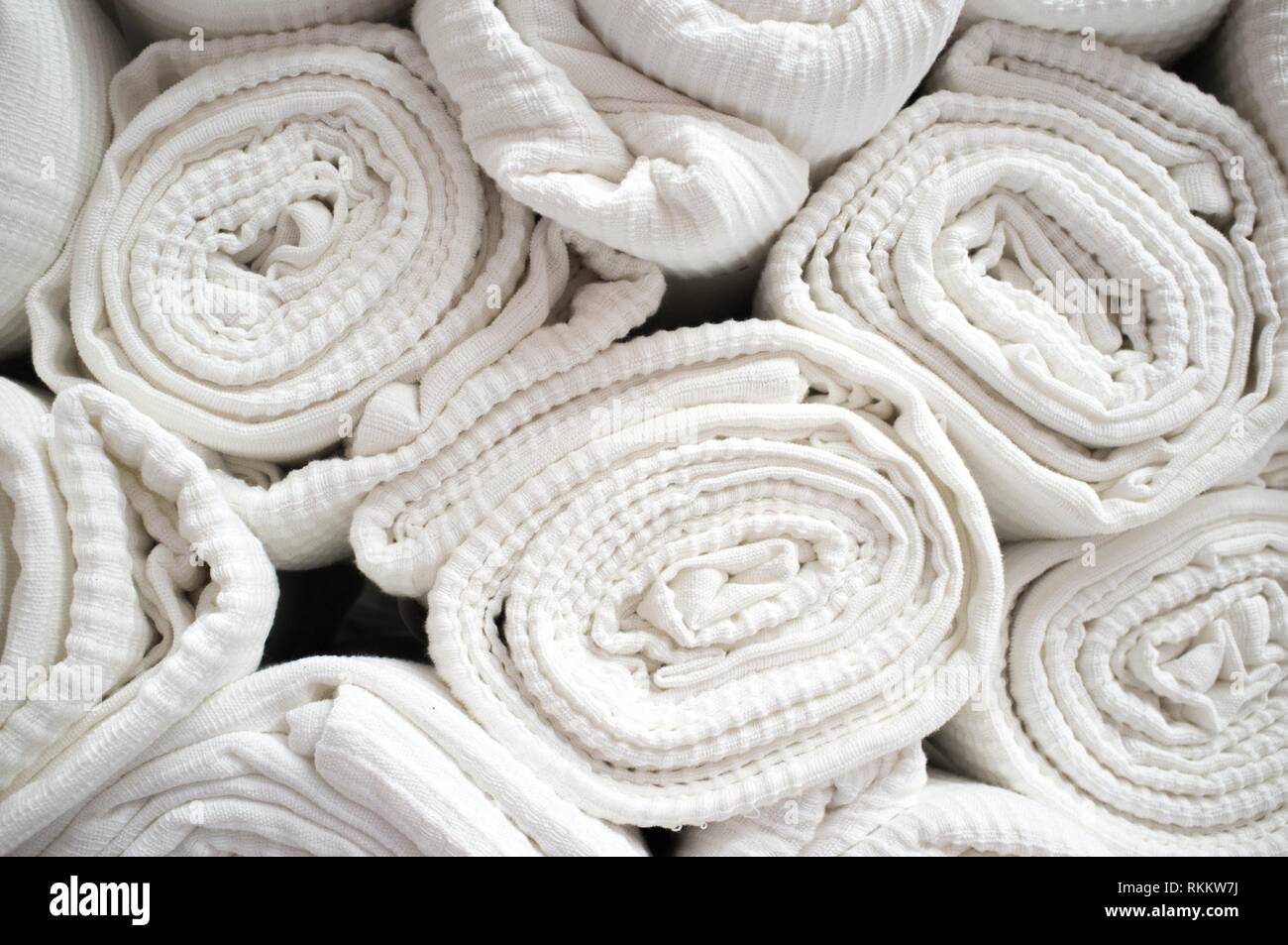 Loads of rolled white cotton bedspreads. Closeup. Stock Photo