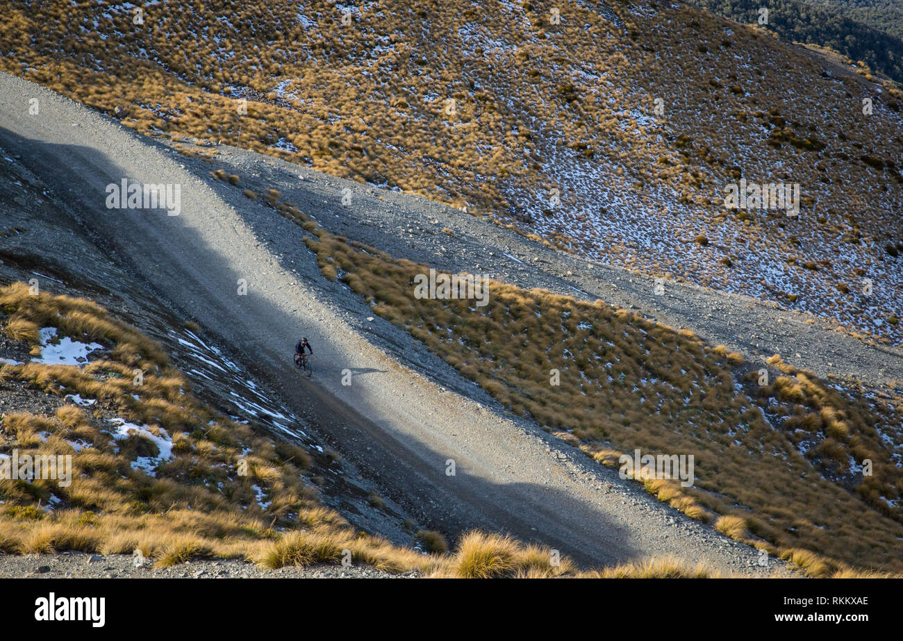 A mountain biker descends the mountain along the ski field road on a frosty morning in Canterbury, New Zealand Stock Photo