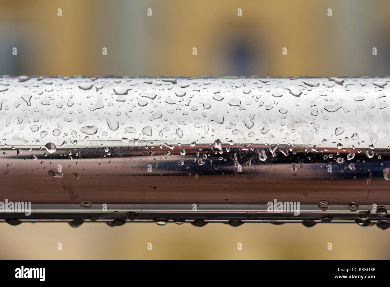 Close-up of horizontal metal wet shiny pipe with big rain water drops on blurred abstract background. Stock Photo