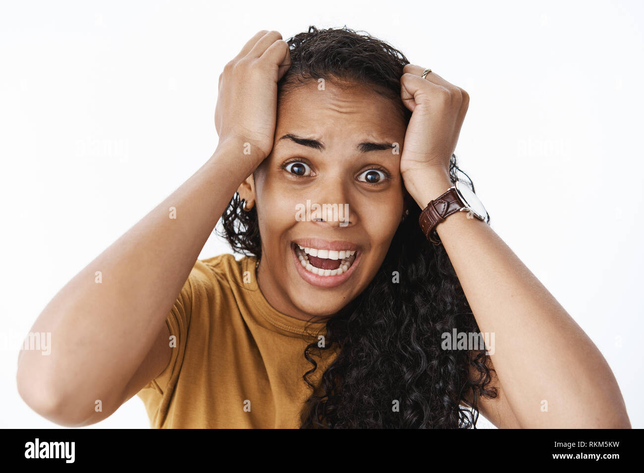 Panicking freaked out african american woman wearing watch and t-shirt screaming shocked and scared holding hands on head popping eyes at camera Stock Photo