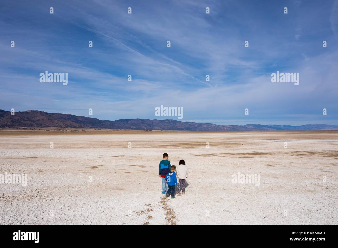 Three young kids run across the mineral and salt flats of the dry lake bed at Middle Alkali Lake near Cedarville California. Stock Photo