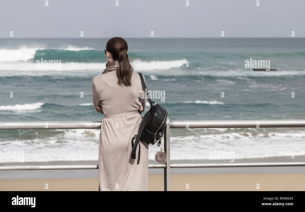 Rear view of smartly dressed young woman looking out to sea Stock Photo