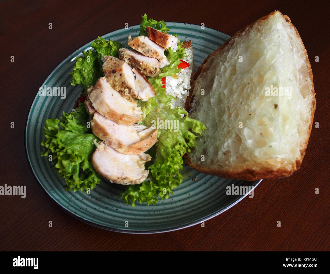 On a large plate lies a sandwich of rustic bread with chicken fillet on