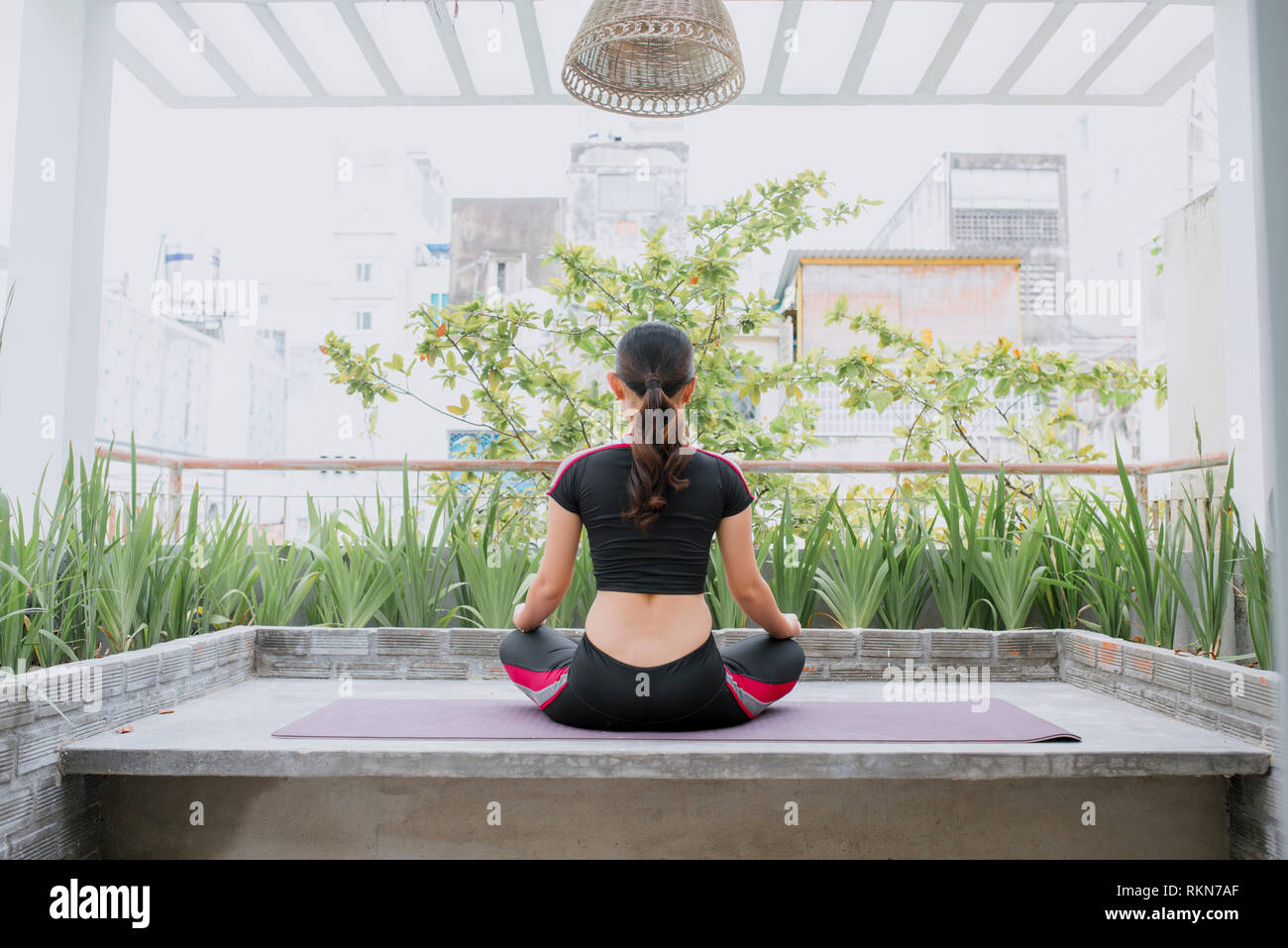 The beautiful woman practicing yoga on a rug and sitting on a balcony