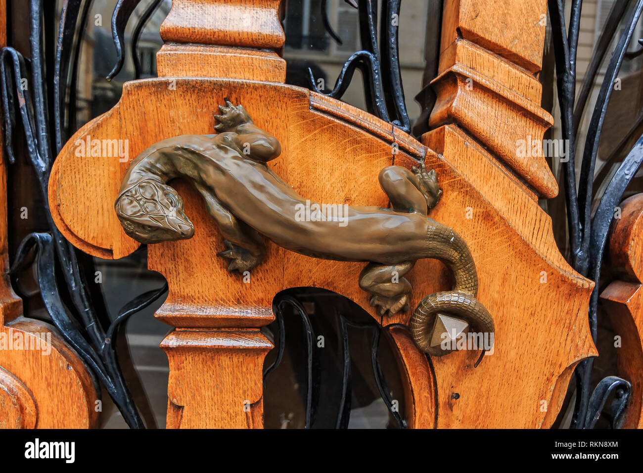 Ornate art nouveau wooden door detail with organic motif and a bronze figurine of a lizard shaped door handle in Paris, France Stock Photo