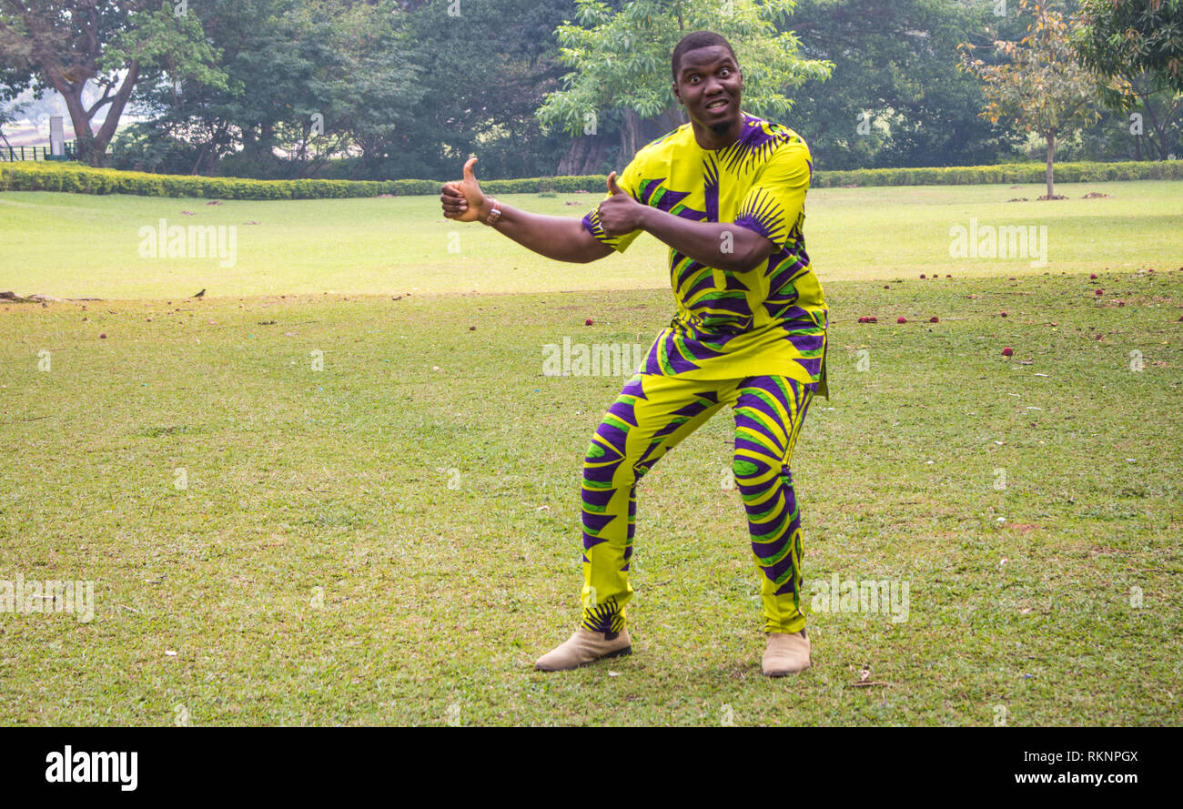 An african male in an open field of green grass and clear skies presents imaginary products or service. Stock Photo