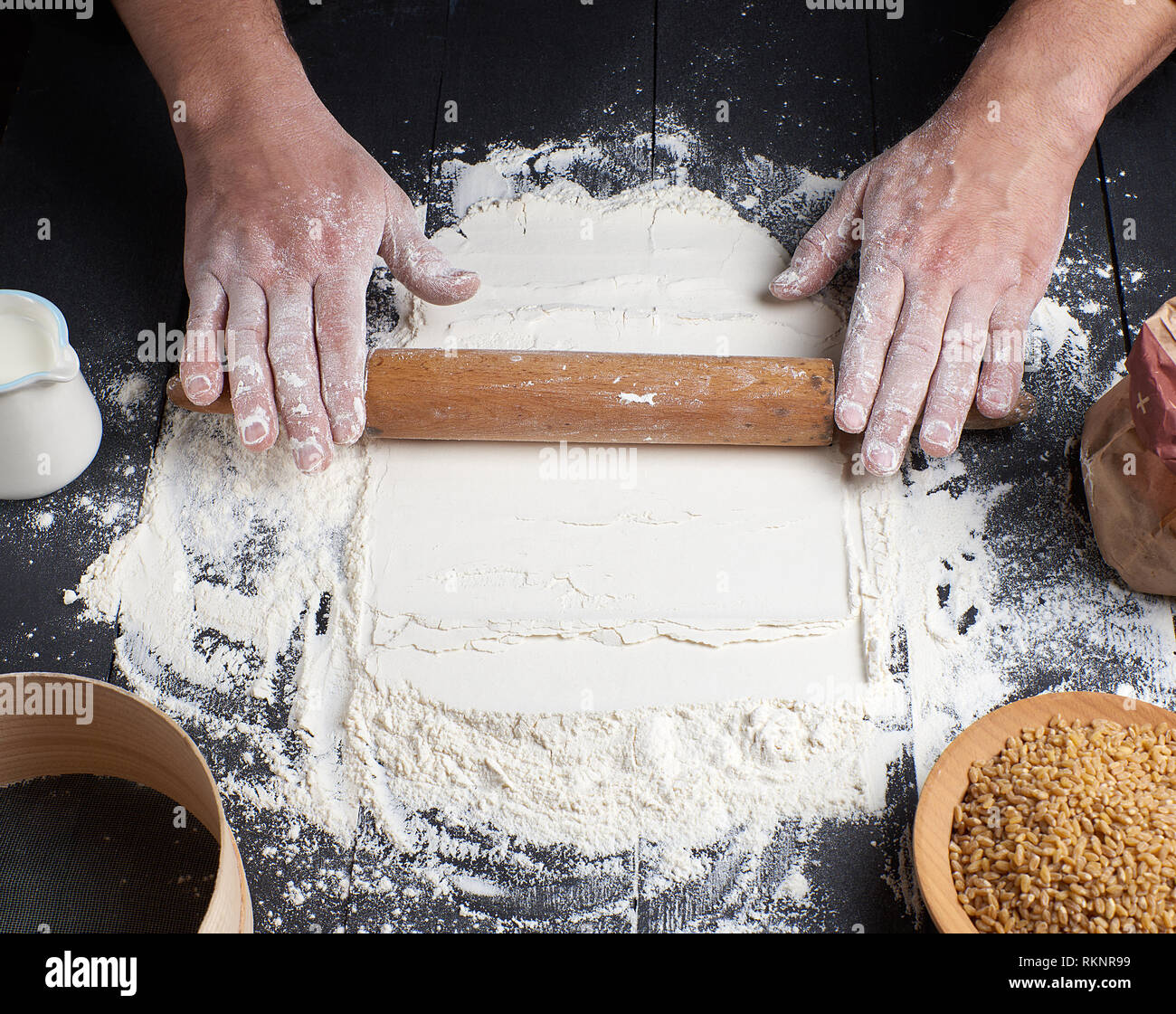 wooden rolling pin in male hands, next is scattered white wheat flour