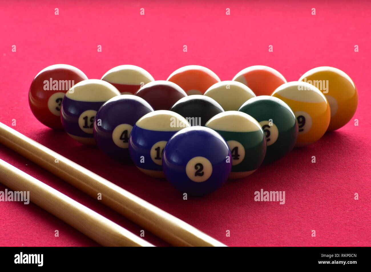 Numbered billiard balls with two pool cues on a red felt table. Stock Photo
