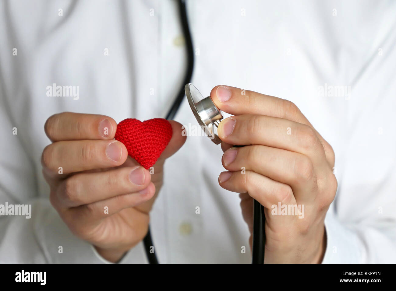 Doctor with stethoscope and red knitted heart in hand. Concept of cardiology, heart diseases, diagnosis, auscultation, medical exam Stock Photo