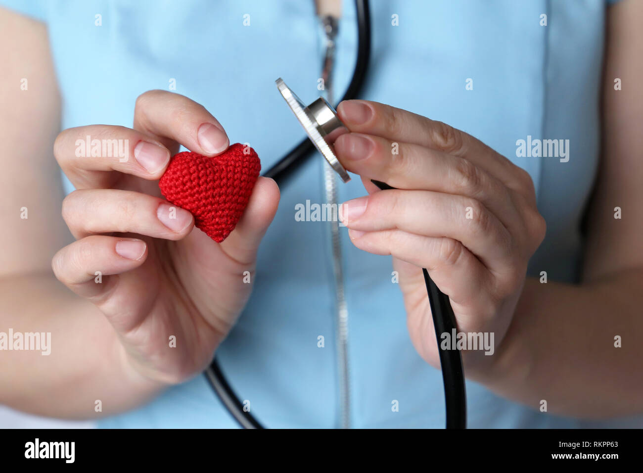 Woman doctor with stethoscope and red knitted heart in hand. Concept of cardiologist, heart diseases, diagnosis, auscultation, medical exam Stock Photo