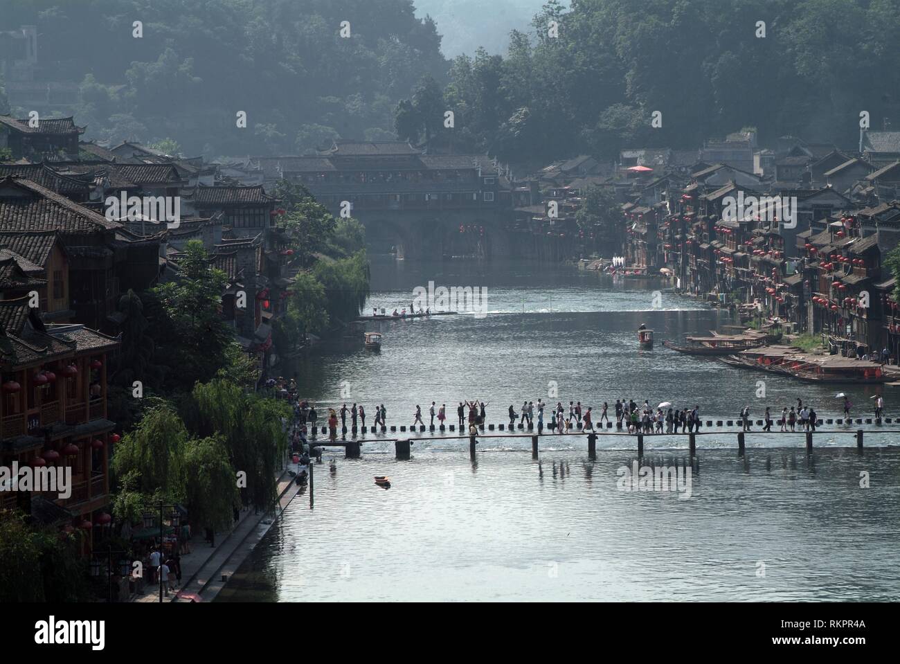 People crossing the Tou Jiang River by stepping stones in Fenghuang. Meaning 'Phoenix' in Chinese, Fenghuang was named after the mythical bird of immo Stock Photo