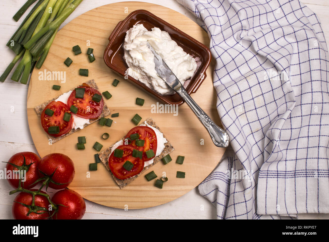 healthy and vegetarian breakfast with crispbread, quark, tomatoes and spring onions on a wooden board Stock Photo
