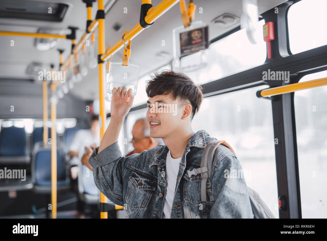 Young asian man is standing in the bus using phone and holding onto the bar while waiting to arrive at her destination. Stock Photo