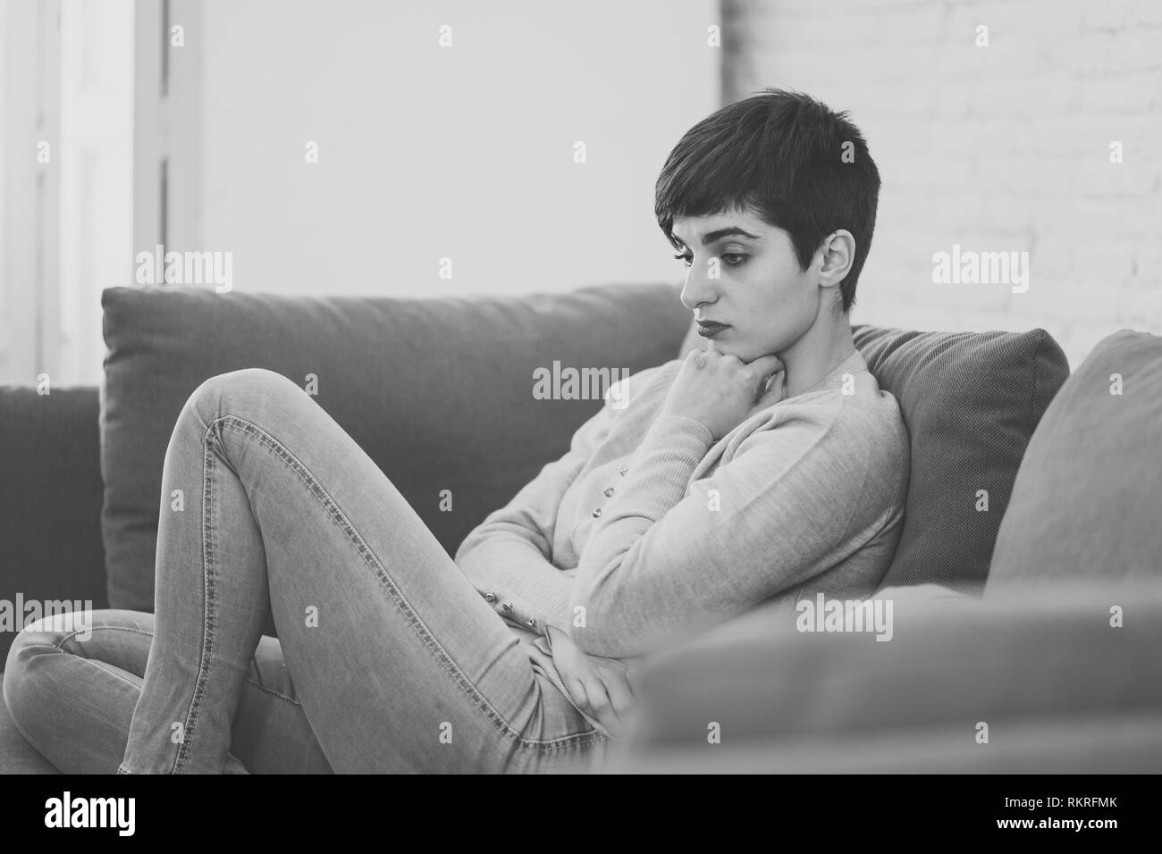 Black and white portrait of attractive, desperate and depressed young woman on sofa feeling sad, hopeless suffering from depression in pain. People, M Stock Photo