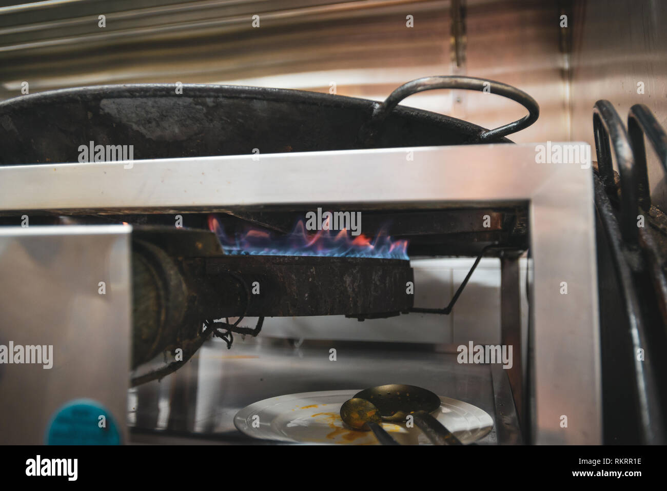 The flame on a gas stove heating a black pan of paella in a restaurant