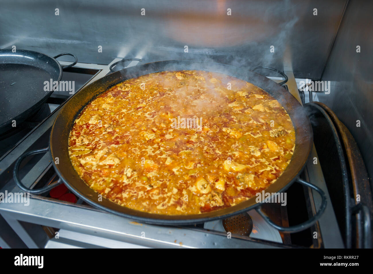 Paella cooking in a black pan on the top of a gas stove in a restaurant kitchen in Valencia, Spain. Stock Photo