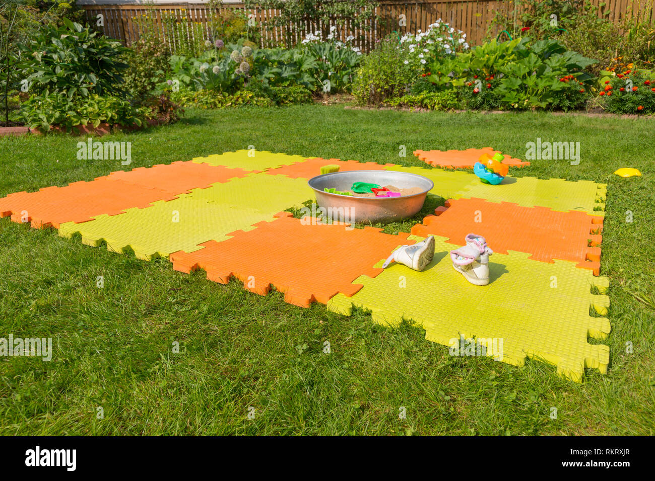 Color children's mat on the green grass in the country. Porous orange foam mat carpet. Children's shoes in the foreground Stock Photo