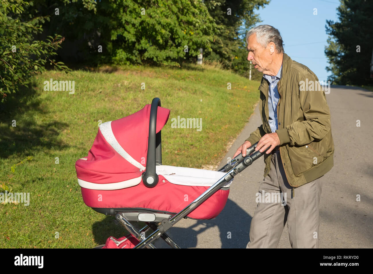 Grandfather carries granddaughter in pink baby carriager at sunset. Outdoor in the country. Stock Photo