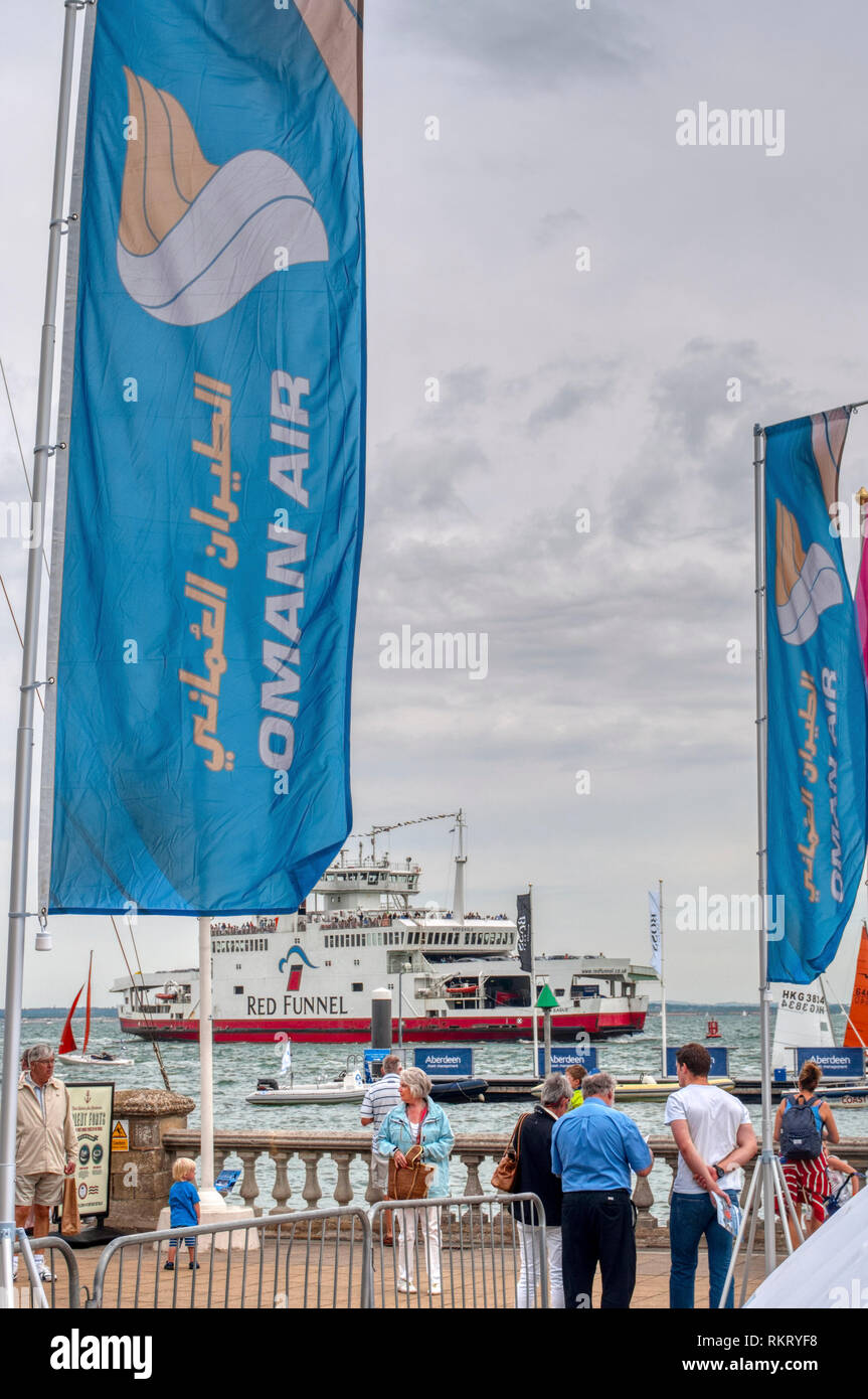 Cowes Week 2013  Isle of Wight, onshore Oman Air banner ads, people walking standing talking on shoreline, UK Stock Photo