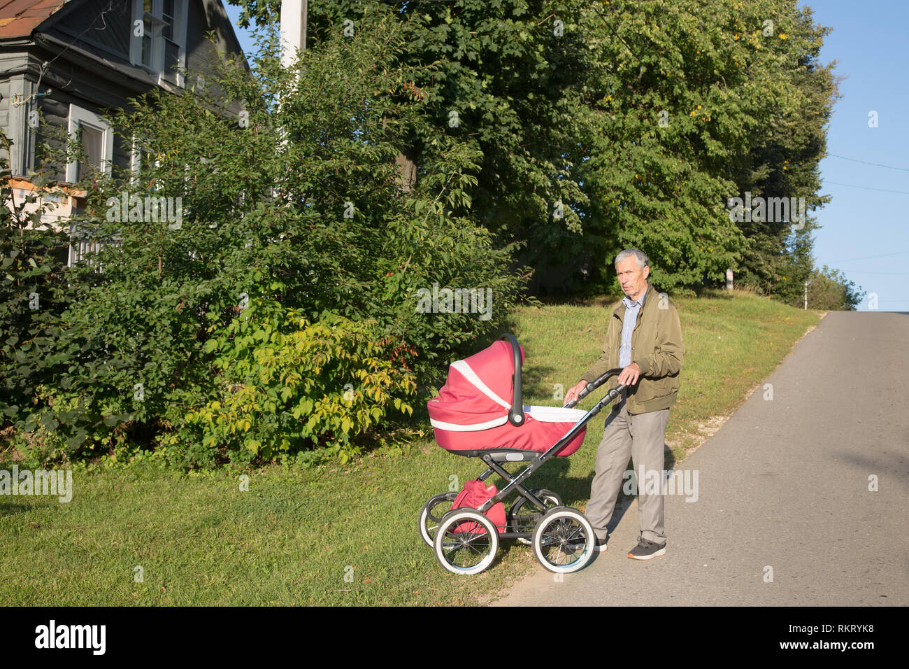 Grandfather carries granddaughter in baby carriager at sunset. Outdoor in the country. Stock Photo