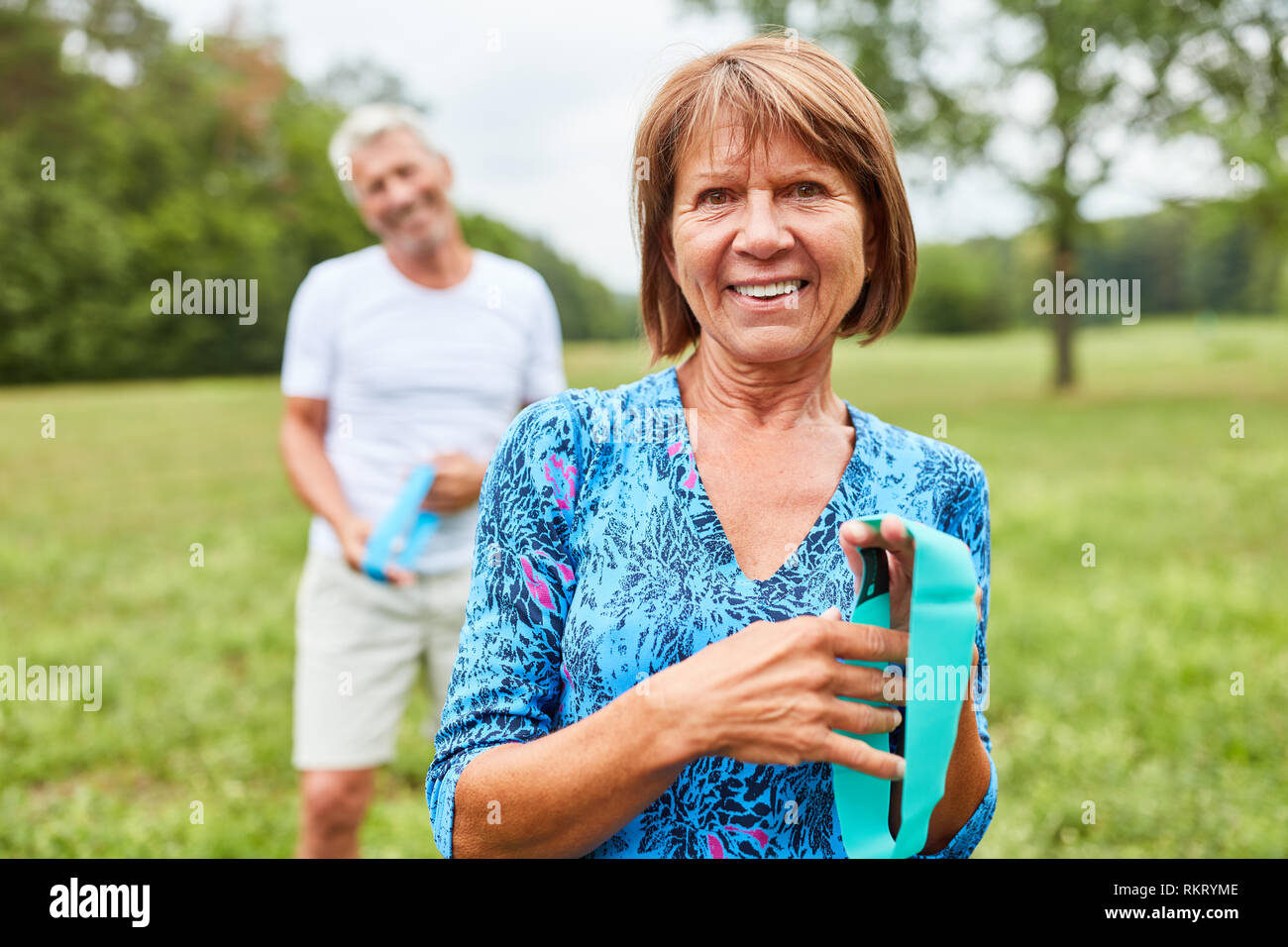 Active senior woman and her partner doing rehab training with stretch band in nature Stock Photo