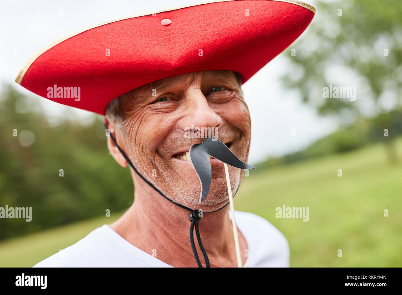 Senior man at a masquerade ball or carnival with red hat and beard Stock Photo