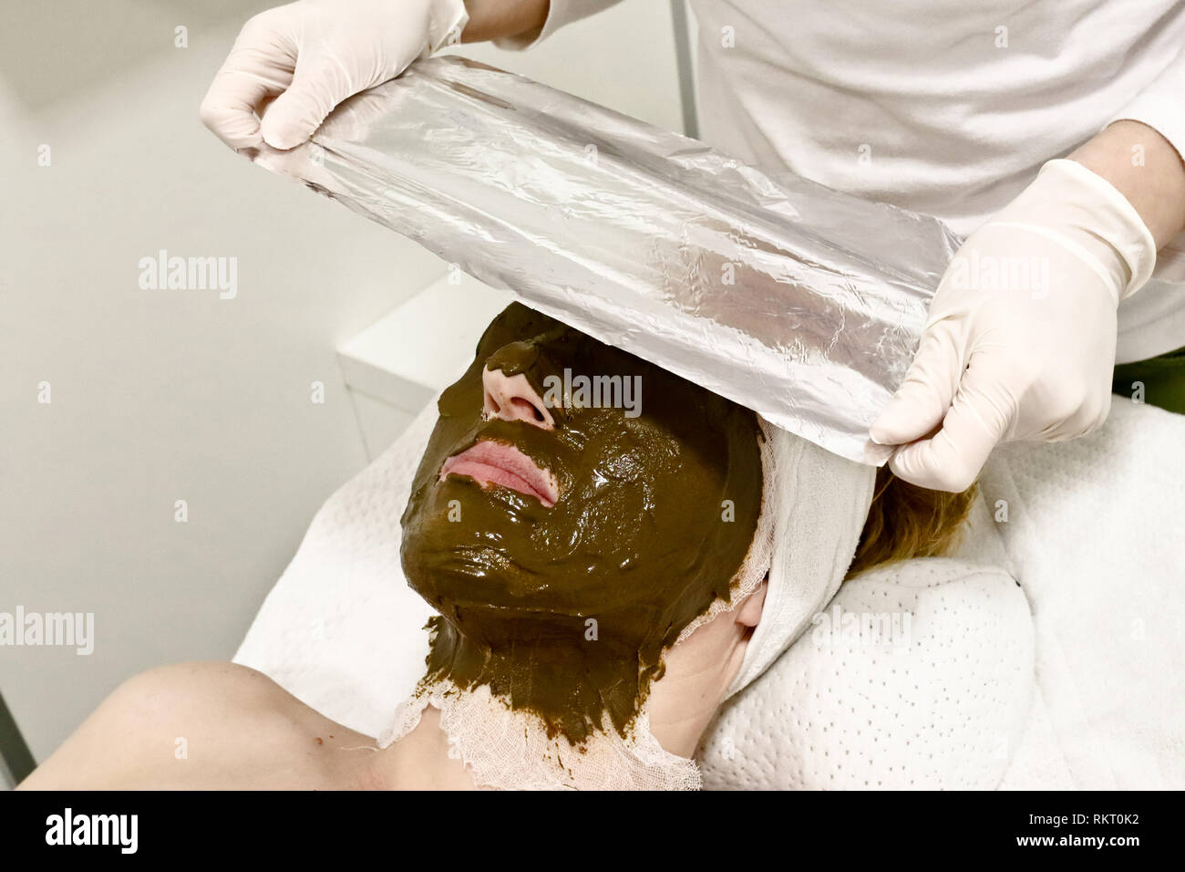 beautician worker puts aluminum foil on female customer face, procedure after applying cosmetic facial mask of sea algae Stock Photo