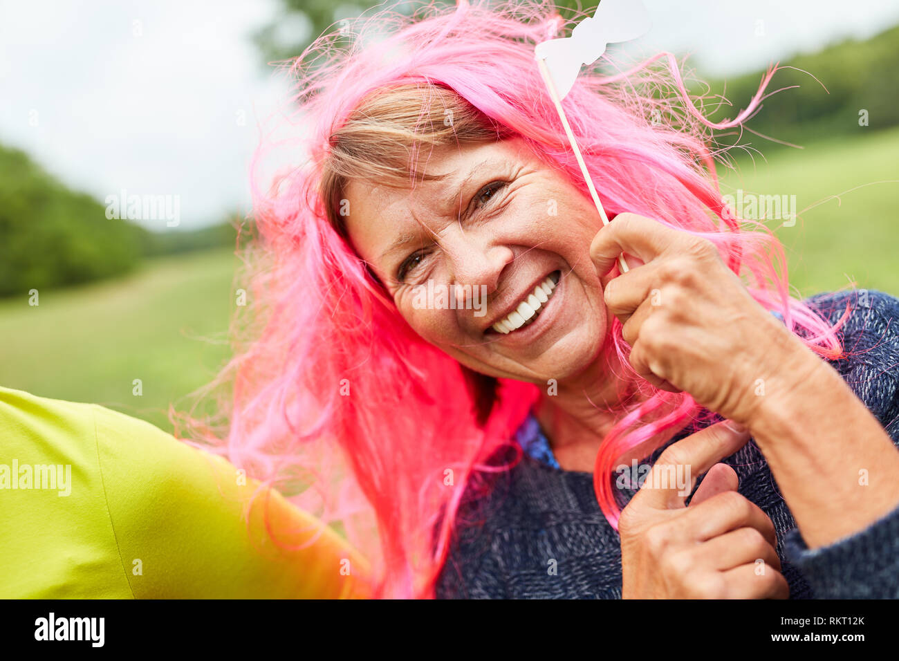 Cheerful senior woman with pink wig on a costume party or masquerade ball Stock Photo