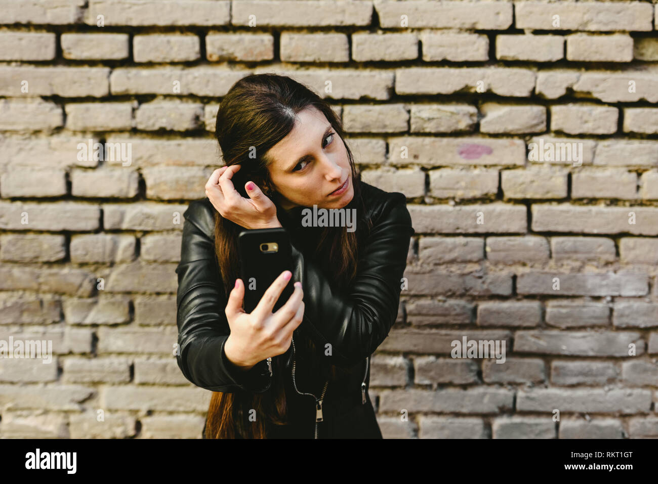 Young girl using the screen of her mobile phone as a mirror to put on makeup and remove pimples from her face, and she gets pretty for a date with her Stock Photo