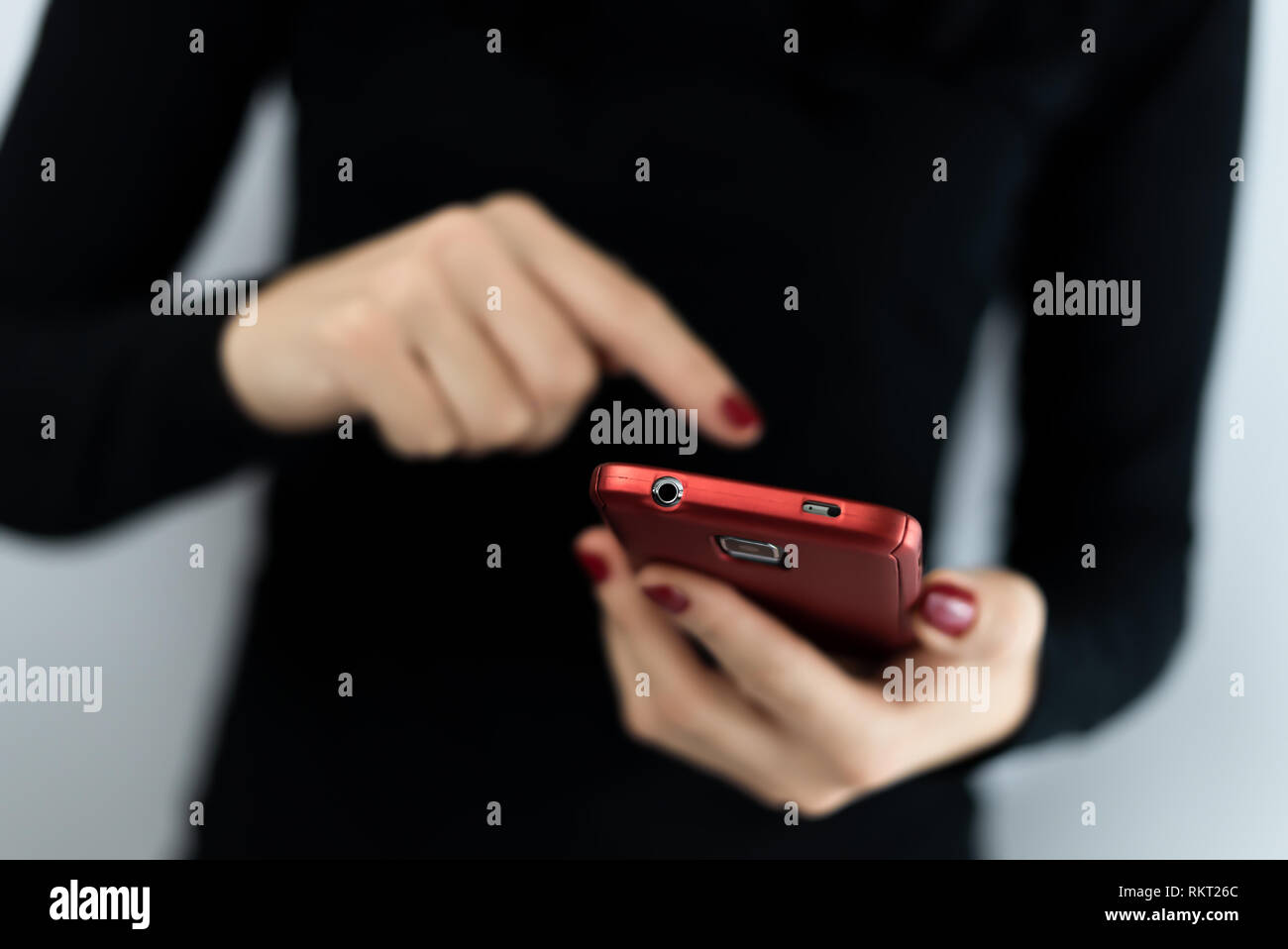 Closeup detail of young woman holding a red cell phone with camera using a touchscreen with apps to connect on social media, texting and chatting Stock Photo