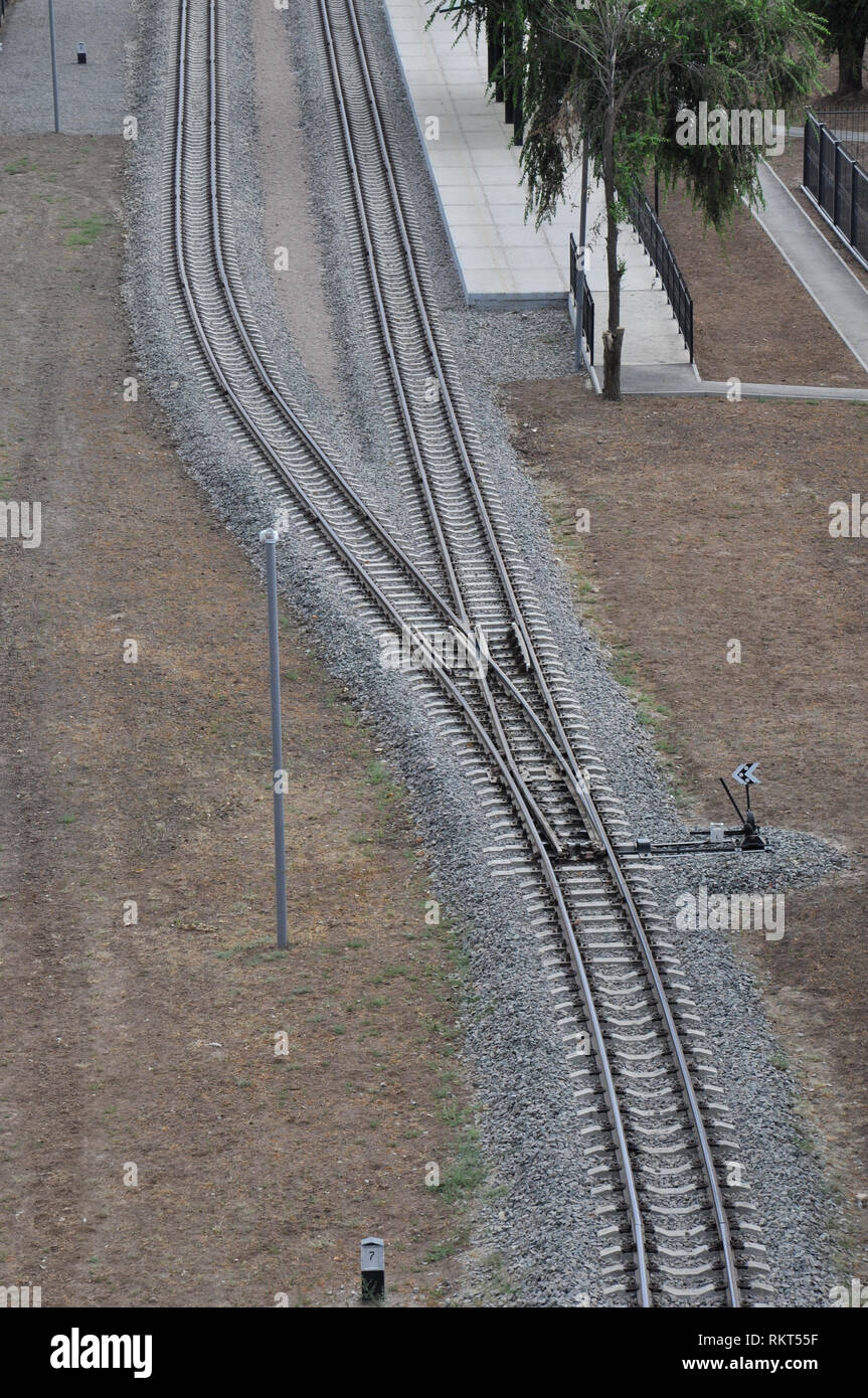 Aerial view of forking railway tracks with posts and tidy platform under green trees. Stock Photo