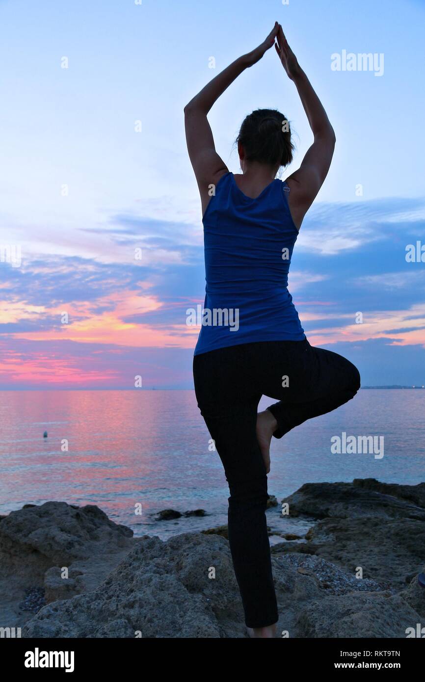 Yoga asana - tranquil meditation exercise with sunset view of Italian coast. Vrikshasana - tree pose. Stock Photo