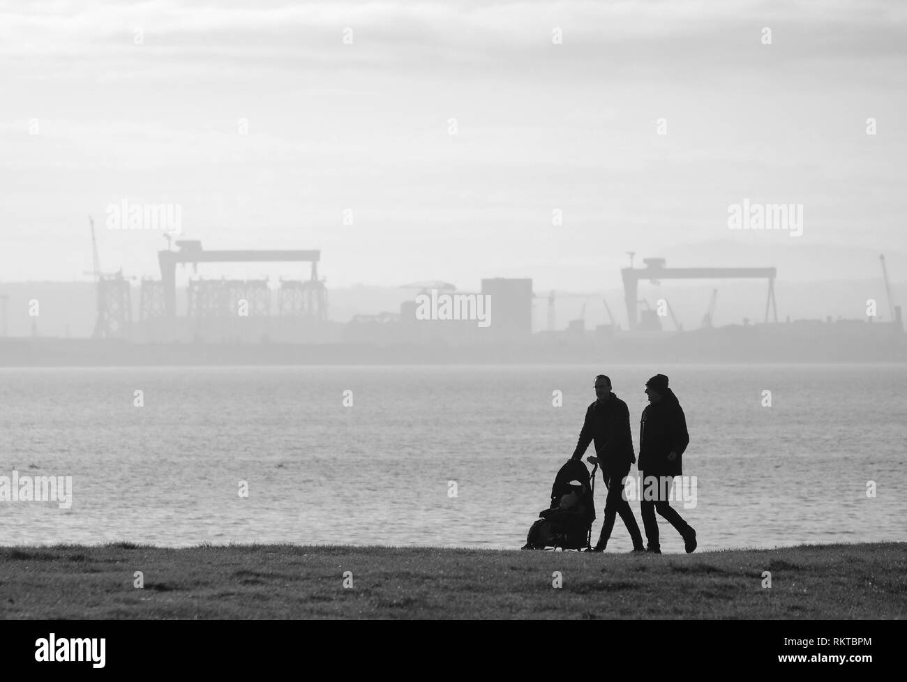 Young couple with child, Loughshore Park, Belfast; (Harland & Wolff shipyard in the distance). Stock Photo