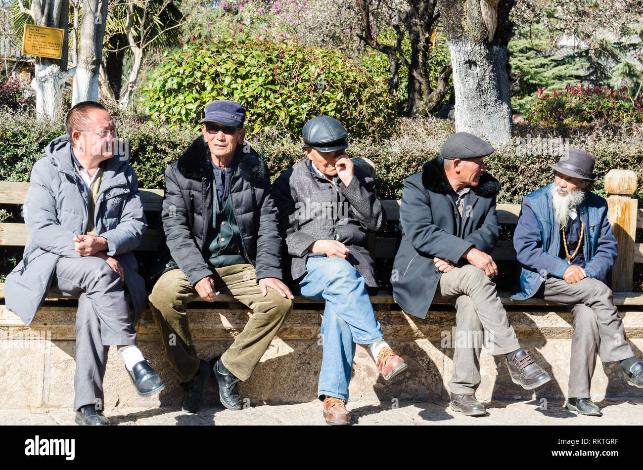 Group of Chinese old men sitting in line on a bench in Yuhe square, Lijiang old town, Yunnan, China Stock Photo